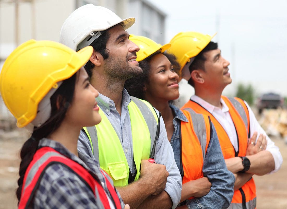 Contact - Diverse Group of Smiling Contractors and Engineers Looking Ahead While Standing with Their Arms Folded at a Construction Jobsite