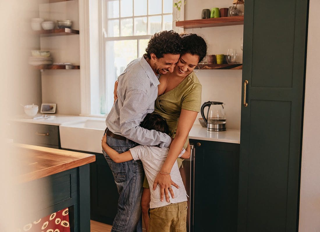 Personal Insurance - Portrait of a Cheerful Mother and Father Standing in the Kitchen While Being Hugged Closely by Their Younger Son